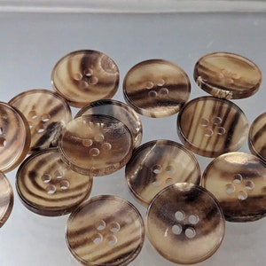 Può includere: Una collezione di bottoni marroni e beige con un motivo a spirale e quattro fori ciascuno. I bottoni sono realizzati in un materiale naturale, possibilmente corno o osso.