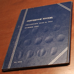 May include: A blue Jefferson Nickel collection album. The cover features the text "Jefferson Nickel Collection 1938 to 1961 Number One" in white. The album has a textured surface and a decorative white border.