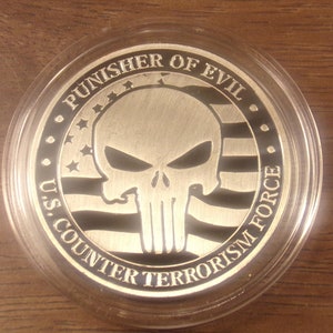 May include: Silver-colored coin featuring a skull design with the words "PUNISHER OF EVIL" and "U.S. COUNTER TERRORISM FORCE." The coin has an American flag design and is encased in a clear plastic holder.