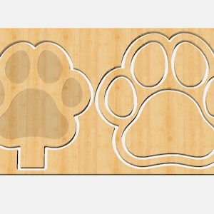 May include: Two wooden paw prints cutouts on a light brown wooden background. The paw prints are outlined in white.
