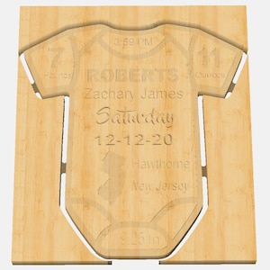 May include: A wooden cutout of a baby onesie with the text "ROBERTS Zachary James Saturday 12-12-20 Hawthorne New Jersey 7 pounds 11 ounces 19.25 in" engraved on it.