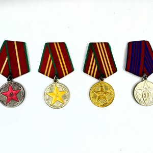 May include: Four vintage medals with colorful ribbons. The medals feature star and circular designs, with red, yellow, and blue accents. The ribbons are red, yellow, and blue with gold stripes. A collectible item.