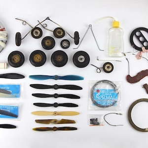 Peut inclure: Ensemble de pièces détachées d'avions modèles anciens, comprenant des roues, des hélices, une bouée de sauvetage et une bouteille. Les pièces sont de couleurs variées, dont le noir, le marron et le bleu.