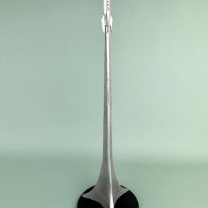 May include: A silver metal rocket model with the text "CCCP" in red. The rocket sits atop a long, slender stand that flares out to a star-shaped base. The base is a black circle.