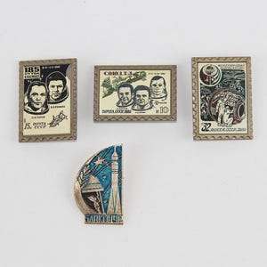 May include: A collection of vintage Soviet space-themed pins and stamps. The stamps feature portraits of cosmonauts and space-related imagery. The pin has a blue and silver design with the text "BAIKONUR".