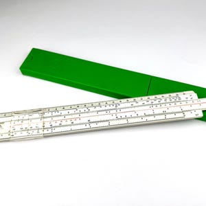 May include: A vintage slide rule with white and black markings, partially extended from a bright green case. The slide rule is a mathematical tool used for calculations. The case is rectangular and has a simple design.