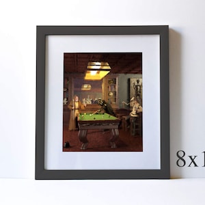May include: A framed illustration of a pool room with two figures playing pool. The room is dimly lit with a single light fixture above the pool table. The pool table is green with white balls and a cue stick. The figures are dressed in casual clothing. The frame is dark gray with a white mat.