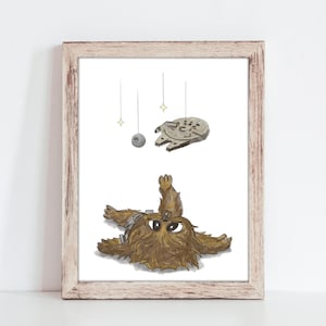 May include: A framed illustration of a brown Wookiee character from Star Wars lying on its back with its arms raised, looking up at a hanging mobile with a silver Death Star and a gray X-Wing spaceship. The mobile is suspended from the ceiling with strings.