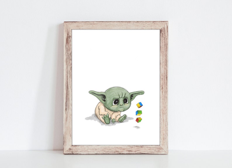 May include: A framed print featuring a watercolor illustration of a baby alien with large eyes and pointed ears. The alien is sitting and looking down, with three colorful toy blocks nearby. The frame is made of light-colored wood.