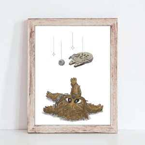 May include: A framed print featuring a whimsical illustration of Chewbacca lying down, with the Millennium Falcon, a Death Star, and stars suspended above. The artwork is in a cartoon style with a light brown wooden frame.