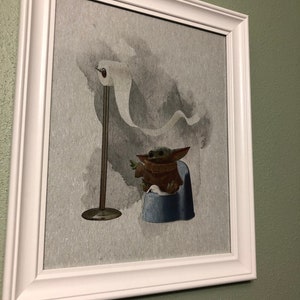 May include: A framed print of a green alien character sitting on a blue potty with a roll of toilet paper hanging in the background.