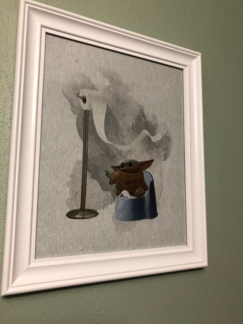 May include: A framed print of a green alien character sitting on a blue potty with a roll of toilet paper hanging in the background.