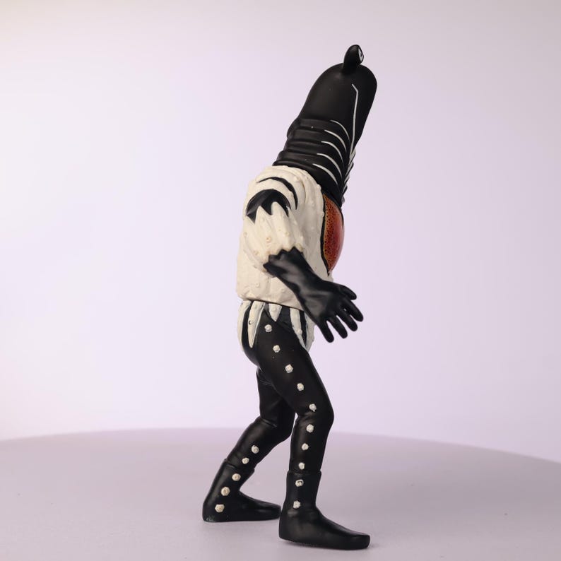May include: A black and white action figure of a humanoid creature. The figure has a black head and body, with a white and cream-colored torso and black gloves. The legs are black with white accents.