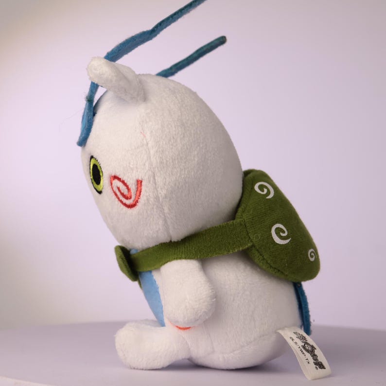 Puede incluir: Un peluche blanco con vientre azul y dos largas antenas azules. Presenta una mochila verde en forma de caparaz&oacute;n con patrones de espirales blancas, una marca de espiral roja en la mejilla y un ojo amarillo con una pupila negra.