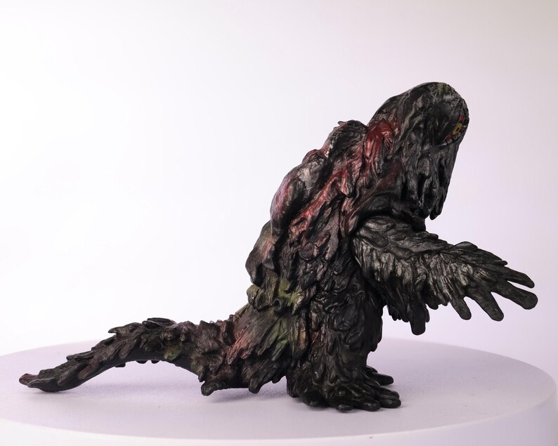 Puede incluir: Figura detallada, pintada a mano, de una criatura con un cuerpo oscuro y texturizado. La figura tiene una postura encorvada, con una larga cola y brazos extendidos. Los acentos rojos y verdes a&ntilde;aden color.