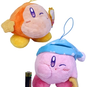 May include: Two plush toys, one orange and one pink, with smiling faces and winking eyes. The orange toy has a star-shaped hand and a yellow loop. The pink toy wears a blue nightcap. A Panasonic AA battery is next to the toys.