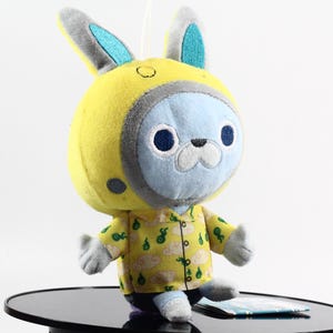 May include: A plush toy with a blue face and yellow and green clothing. The toy has bunny ears and a yellow helmet with a grey visor.