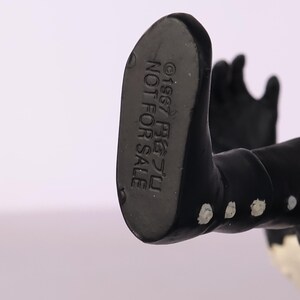 May include: Close-up of the underside of a black figurine's foot. The text "&copy;1967 尾芝フミ NOT FOR SALE" is printed on the foot. The figurine is black with white accents.