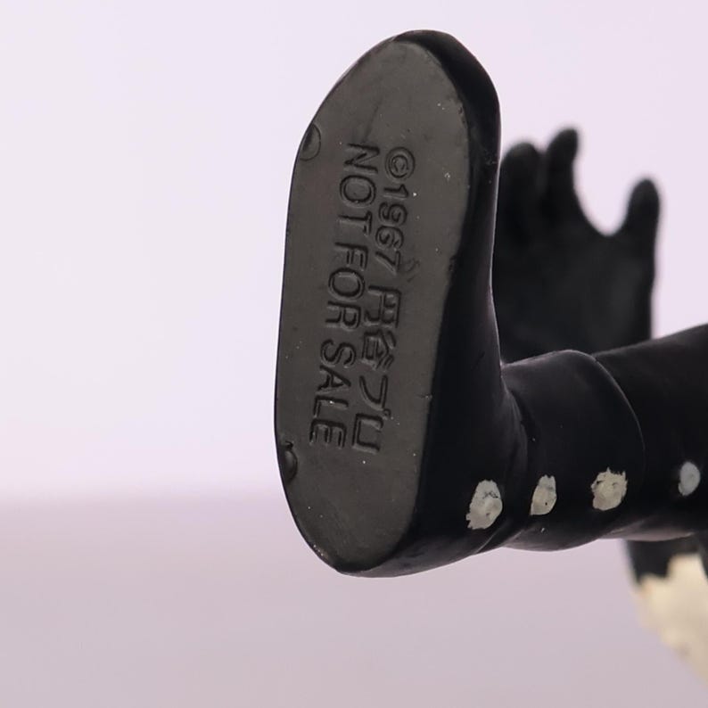 May include: Close-up of the underside of a black figurine's foot. The text "&copy;1967 尾芝フミ NOT FOR SALE" is printed on the foot. The figurine is black with white accents.