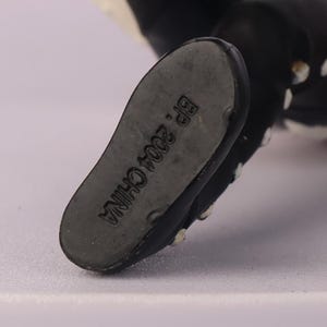 May include: Close-up of the sole of a black and white figurine's foot. The sole is gray and has the text "BP. 2004 CHINA" printed on it. The figurine's foot is black with white dots.
