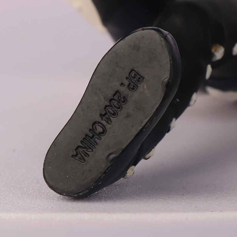 May include: Close-up of the sole of a black and white figurine's foot. The sole is gray and has the text "BP. 2004 CHINA" printed on it. The figurine's foot is black with white dots.