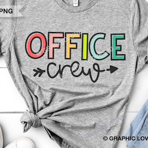 May include: A gray t-shirt with the text "OFFICE crew" in rainbow colors. The text is outlined in black and has arrows on either side.