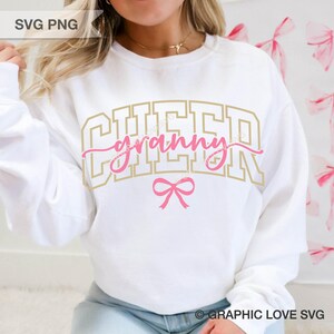 May include: White sweatshirt with the text "CHEER granny" in gold and pink lettering, with a pink bow graphic. The sweatshirt is a crew neck style.
