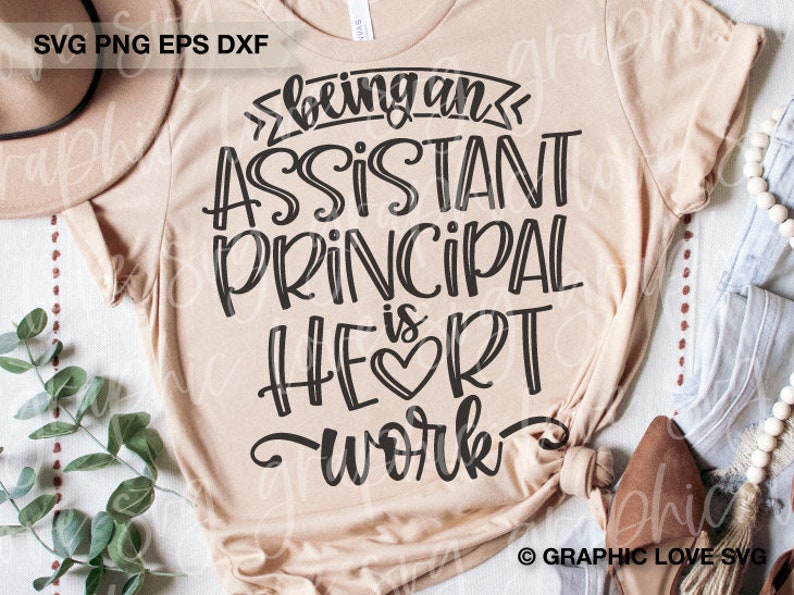 May include: A beige t-shirt with the text "Being an Assistant Principal is Heart Work" in black lettering. The text is in a stylized font with a heart symbol in the word "Heart".