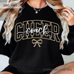 May include: Black sweatshirt with the word "CHEER" in a gold outlined block letter font, with the word "coach" in a white script font. A gold bow is below the word "coach". The sweatshirt is a cheerleading or coaching themed design.