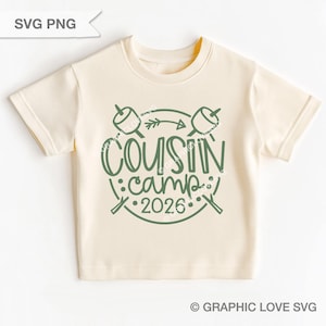 Puede incluir: Camiseta color crema con un gráfico verde que dice "Cousin Camp 2026". El diseño incluye malvaviscos en palitos, una flecha y un tema de campamento. La camiseta es de material suave.