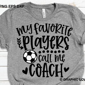 May include: Gray t-shirt with black text that reads "My favorite players call me coach" with a black and white soccer ball graphic and two black hearts.
