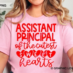 May include: Pink t-shirt with the text "Assistant Principal of the cutest sweet hearts" in red. The text is surrounded by red hearts.