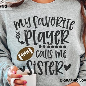 Puede incluir: Sudadera gris con el texto "Mi jugador favorito me llama hermana" y un gráfico de fútbol americano marrón.