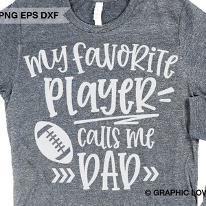 May include: Gray t-shirt with white text that reads "my favorite player= calls me DAD" with a white football graphic. The text is in a handwritten font.