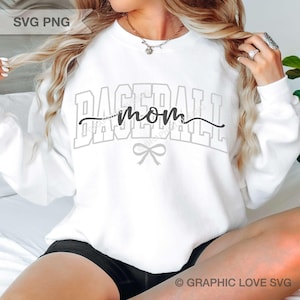 May include: A white long-sleeve sweatshirt featuring the word BASEBALL in large light gray outlined block letters. Overlaid in black script is the word mom, accompanied by a small gray bow graphic centered below the text on the chest.