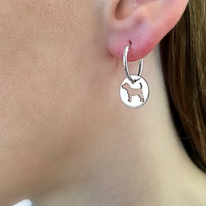 Puede incluir: Pendientes de aro de plata con un dije colgante que presenta una silueta recortada de un perro.