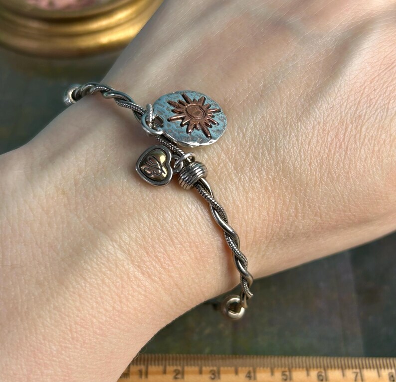 Pu&ograve; includere: Un braccialetto in argento e rame con un ciondolo a forma di sole e un ciondolo a forma di cuore. Il braccialetto &egrave; intrecciato e ha un design delicato.