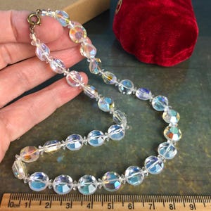 Puede incluir: Un collar de cristal transparente con cuentas iridiscentes. El collar está hecho de cuentas facetadas de forma ovalada y tiene un cierre plateado.