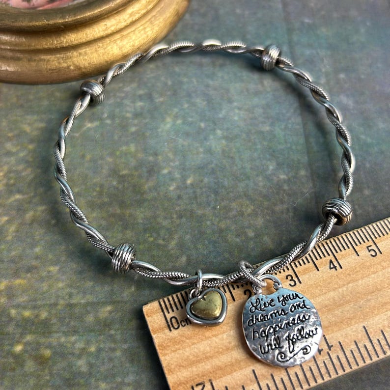 Pu&ograve; includere: Braccialetto in argento intrecciato con un ciondolo a forma di cuore e un ciondolo rotondo che dice "Live your dreams and happiness will follow".