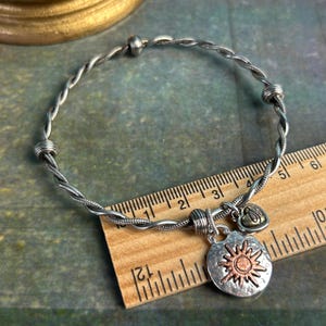 Pu&ograve; includere: Braccialetto in argento intrecciato con un ciondolo a forma di sole e un ciondolo a forma di cuore. Il braccialetto &egrave; lungo circa 17,8 cm.