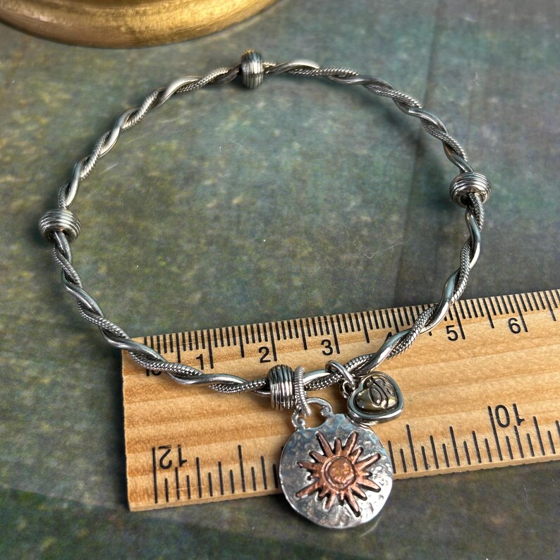 Pu&ograve; includere: Un braccialetto in filo d'argento intrecciato con due ciondoli. Un ciondolo &egrave; un sole d'argento con un centro in rame e l'altro &egrave; un piccolo cuore d'oro. Il braccialetto viene misurato con un righello.