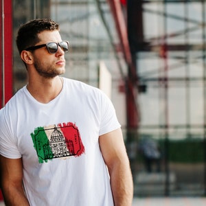 Peut inclure: Un t-shirt blanc avec un imprim&eacute; graphique du Colis&eacute;e &agrave; Rome, en Italie. Le graphique est en noir et blanc et pr&eacute;sente un sch&eacute;ma de couleurs vert, blanc et rouge rappelant le drapeau italien.