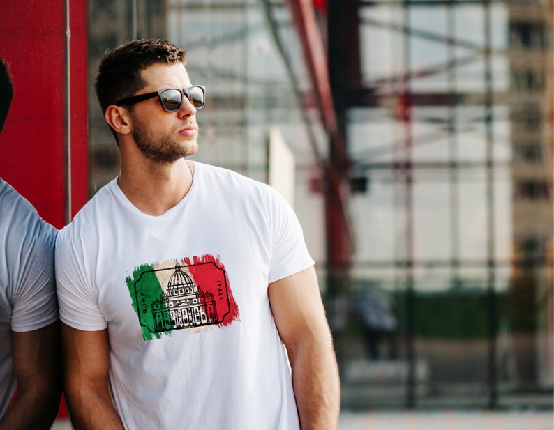 Peut inclure: Un t-shirt blanc avec un imprim&eacute; graphique du Colis&eacute;e &agrave; Rome, en Italie. Le graphique est en noir et blanc et pr&eacute;sente un sch&eacute;ma de couleurs vert, blanc et rouge rappelant le drapeau italien.