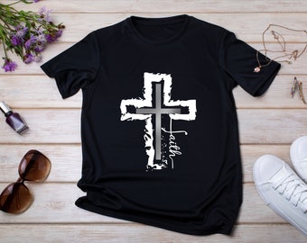 May include: Black t-shirt featuring a distressed white cross design with a gray center and the word "faith" in white script. The shirt is made of a soft, dark fabric, suitable for casual wear. The design is centered on the front of the shirt.