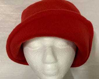 May include: A bright red bucket hat with a soft, felt-like texture and a wide, downward-sloping brim. The hat features a rounded crown and a solid, uniform color throughout, providing a simple and functional design for headwear.