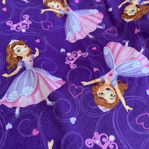 May include: Purple fabric with a repeating pattern of a cartoon princess wearing a pink and purple dress. The princess is holding a crown and has brown hair. The background is purple with pink hearts and swirls.