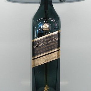 May include: A table lamp made from a Johnnie Walker Double Black Blended Scotch Whisky bottle. The lamp has a black lampshade and a gold base.