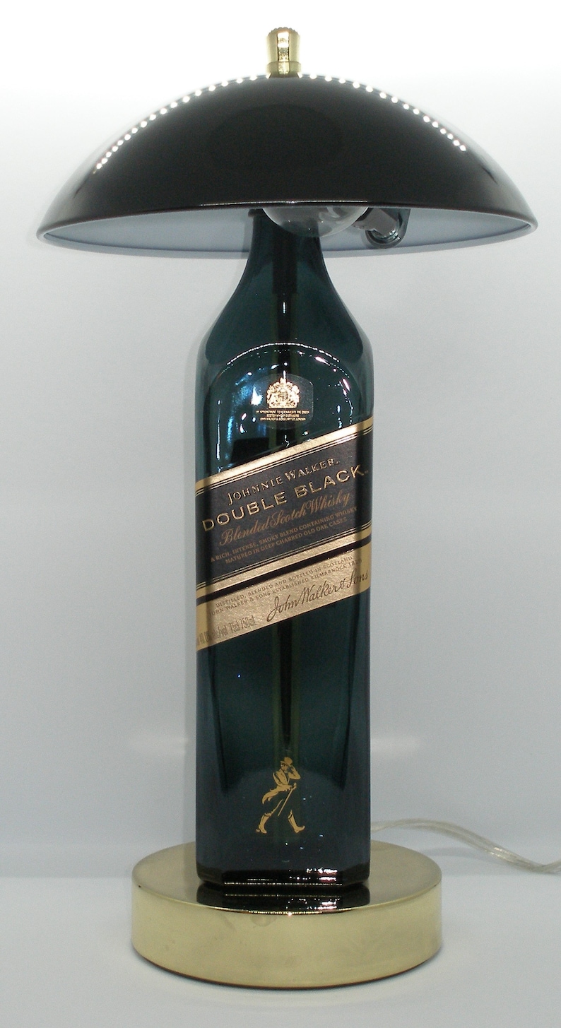 May include: A table lamp made from a Johnnie Walker Double Black Blended Scotch Whisky bottle. The lamp has a black lampshade and a gold base.