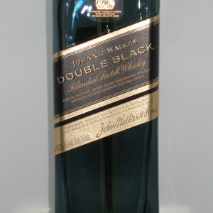 May include: A dark green glass bottle of Johnnie Walker Double Black Blended Scotch Whisky. The label is gold with black text that reads "Johnnie Walker Double Black Blended Scotch Whisky" and "A rich, intense, smoky blend containing whisky matured in deep charred old oak casks". The bottle is 750 ml.
