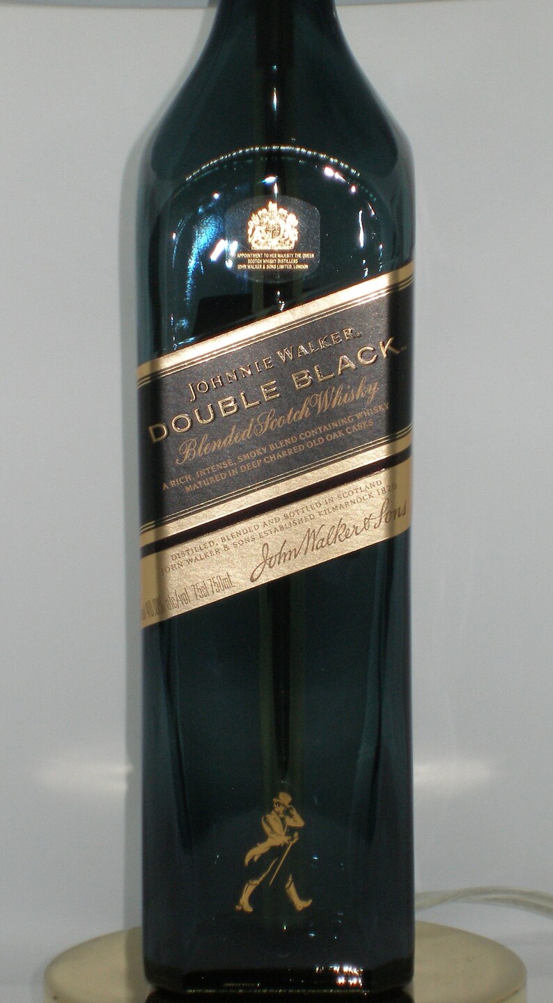 May include: A dark green glass bottle of Johnnie Walker Double Black Blended Scotch Whisky. The label is gold with black text that reads "Johnnie Walker Double Black Blended Scotch Whisky" and "A rich, intense, smoky blend containing whisky matured in deep charred old oak casks". The bottle is 750 ml.